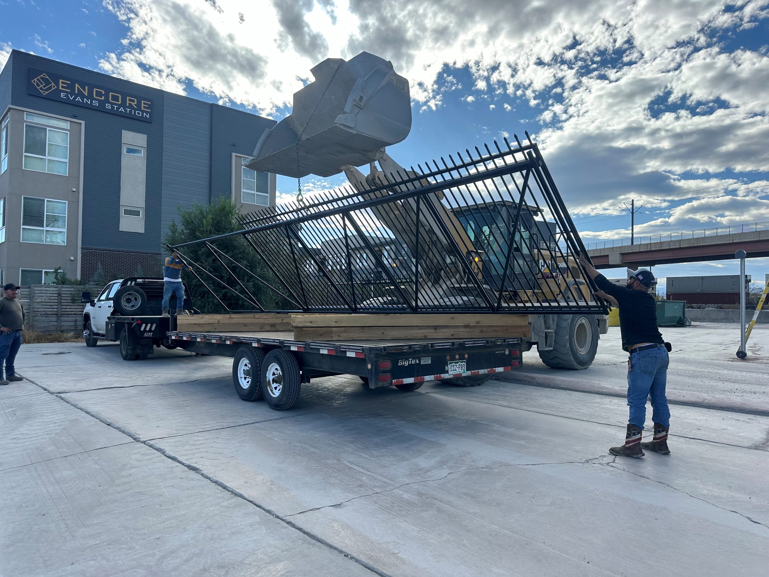 Fence installation crew unloading ornamental metal fence panel at commercial property in Denver Colorado